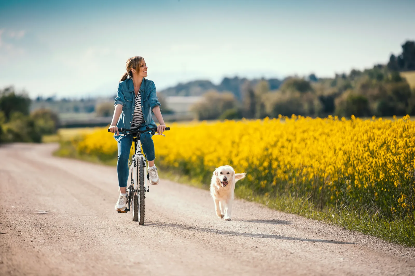 A young woman riding a bike with her dog trotting alongside on a leash