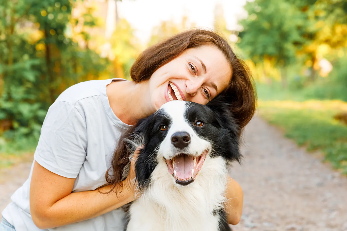 A woman hugging a young Border Collie outdoors in summer