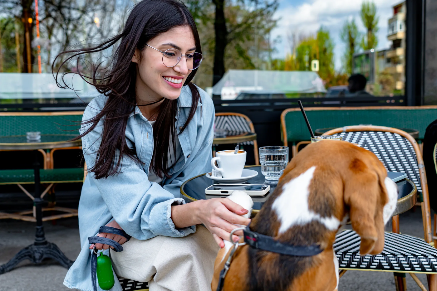 A young woman petting her beagle at an outdoor cafe table